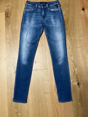 Replay Hyperflex skinny jeans blå - Snygga Replay Hyperflex jeans i klassisk blå tvätt med slitningar och skinny fit. Modellen är New Luz med fem fickor, dragkedja och knapp. Stretchigt material som sitter tajt och bekvämt. Perfekta för dig som gillar en modern och smal siluett.