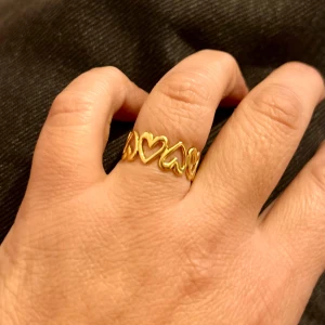 Stål Guldfärgad ring med hjärtan - Superfin stål guldfärgad ring med öppet mönster av flera hjärtan runt hela ringen. Snygg och lekfull design som verkligen sticker ut på fingret. Perfekt accessoar för dig som gillar detaljer med lite extra kärlek. Justerbart ring, kan träffa i Majorna och ibland helgerna i central station 