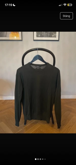 Mörkgrön stickad tröja Tiger of Sweden - Snygg mörkgrön stickad tröja från Tiger of Sweden, modell Matias, tillverkad av fin italiensk garn. Tröjan har rund hals, ribbade muddar och lång ärm. Perfekt för dig som gillar stilrena och klassiska plagg med en modern touch.