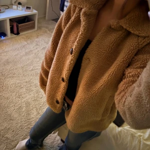 Beige/brun teddyjacka från ONLY - Säljer en beige/brun teddyjacka från ONLY med stora bruna knappar och klassisk krage. Jackan är fluffig och har två sidofickor, perfekt för dig som gillar mysiga och trendiga ytterplagg. Passar dig som vill ha en chill och snygg look.