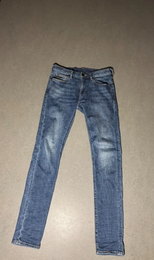Emporio Armani blå jeans straight fit - Snygga blå jeans från Emporio Armani med klassisk femficksdesign och diskret logga på bakfickan. Jeansen har en rak passform och normal midja, tillverkade i mjukt denim med lätt tvättad look och kontrastsömmar. Perfekta för en chill och stilren vibe. 29/34 men sitter som 29:32