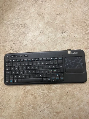 Logitech trådlöst tangentbord med touchpad - Smidigt trådlöst tangentbord från Logitech med inbyggd touchpad och USB-mottagare. Perfekt för smart-TV eller dator. Tangenter och touchpad i gott skick, mindre slitage syns på ytan. Fungerar med de flesta operativsystem.