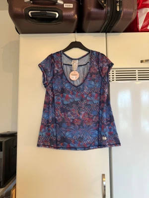 Odd Molly blå sprinter topp mesh - Säljer en sprinter topp från Odd Molly i mörkblå mesh med blommigt mönster i blått och rött. Toppen har korta ärmar, rundad v-ringning och är lätt transparent. Perfekt för dig som gillar färgstarka och unika plagg med sportig vibe. Från märket Odd Molly. Storlek 2 som enligt deras storleksguide motsvarar en M. Helt ny med tags/ prislapp fortfarande kvar. 