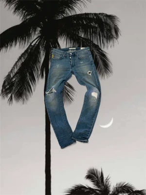  Tramarossa 2020 jeans - Snygga blå jeans från Tramarossa med coola slitningar och hål på benen. Modellen har raka ben, klassisk femficksdesign och detaljer med '2020' på ficka och bak. Jeansen är tillverkade i jeansmaterial och har en modern, streetig vibe.