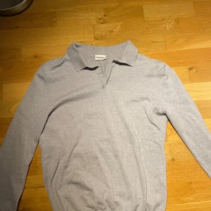 Långärmad pike John Henric merinoull - Snygg grå pikétröja från John Henric i storlek M men passar S. Tröjan har klassisk krage, två knappar vid halsen och långa ärmar. Materialet känns mjukt och skönt mot huden, perfekt för dig som gillar stilrena och enkla plagg. 
