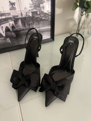 Svarta klackar från Zara - Snygga svarta klackar från Zara med spetsig tå och stor rosett framtill. 
