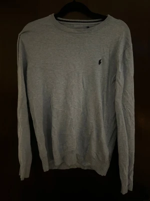 Ljusblå  tröja från Polo Ralph Lauren S - Snygg ljusblå tröja från Polo Ralph Lauren i mjuk pima bomull. Klassisk rund halsringning, ribbade muddar och diskret broderad logga på bröstet. Perfekt för dig som gillar stilren och enkel design.