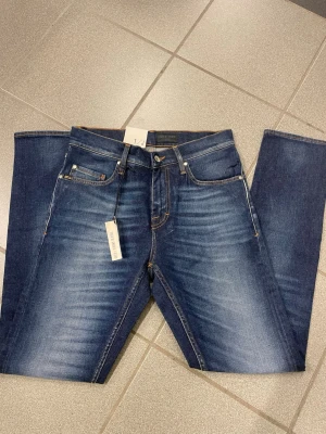 Mörkblå jeans från tiger of Sweden  W28 L32 - Snygga mörkblå jeans från tiger of Sweden . med smal passform och klassisk femficksdesign. Jeansen har kontrastsömmar, läderpatch bak och lätt slitna detaljer framtill. Modellen är straight leg med smal fot, perfekt för dig som gillar stilrena jeans.