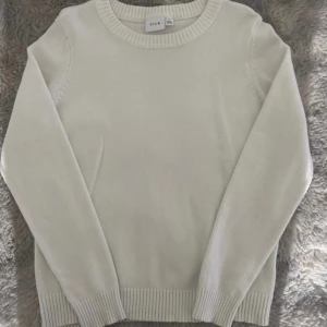 Vit stickad tröja från Vila - Snygg vit stickad tröja från Vila med rund hals och ribbade muddar vid ärmslut och nederkant. Perfekt för dig som gillar enkel och clean stil. Långärmad modell som passar till jeans eller kjol.