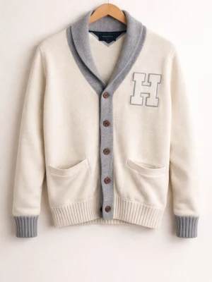 Vit cardigan från Tommy Hilfiger - Säljer en vit och grå kofta från Tommy Hilfiger i storlek M. Koftan har stora bruna knappar, två fickor fram, ribbade muddar och en stor grå krage. Dekorerad med ett stort H på bröstet. Perfekt för dig som gillar college-stil.