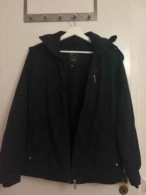 Svart vindjacka från Five Seasons - En svart skid-vind jacka som används för skidåkning men kan också användas allmänt. Är tunn men håller dig varm i de kallaste tiderna! Väldigt skön.  Är storlek M men den passar mig som har storlek XS-S, är bara lite oversized. Köpte för 1000kr.