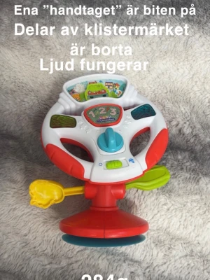 Aktivitetsleksak ratt - Väl lekt med. Ena spaken har varit populär som bitleksak. Klistermärkena har åkt bort lite. Lite färg under. Ljud fungerar 