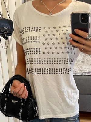 Vit t-shirt med silvriga nitar och stjärnor - En vit t-shirt med coolt tryck av silvriga nitar och stjärnor på framsidan. 