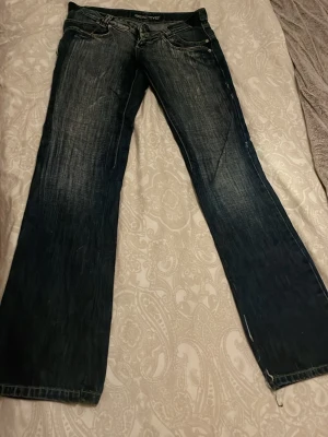 Mörkblå bootcut jeans från Reactive - Säljer ett par mörkblå jeans från Reactive med snyggt slitna detaljer och klassisk femficksdesign. Modellen har bootcut-ben och kontrastsömmar. Jeansen är gjorda i robust denim och har låg midja. Perfekt för dig som gillar en avslappnad stil.