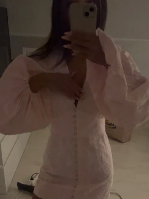 Ljusrosa kortklänning med puffärmar Adoore  - Säljer en ljusrosa kortklänning med stora puffärmar och knappar längs hela framsidan. Klänningen har en feminin v-ringning och är tillverkad i ett lätt, strukturerat tyg som ger en elegant känsla. Perfekt för dig som gillar romantisk och trendig stil.💓💓