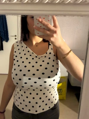 Prickig vit linnetopp från newyourker - Säljer en vit linnetopp från newyourker i storlek M med svarta prickar. Toppen har en snygg omlott-look vid axeln och en stor rosett på ena axeln. Materialet är mjukt och lätt polyester, perfekt för varma dagar. Supersöt och trendig design!