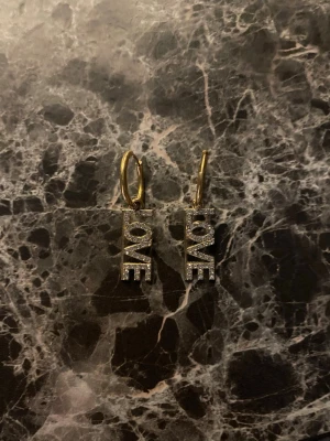 Stockholmsstil örhängen med LOVE-text💞💞 - Säljer ett par snygga örhängen i guldfärg där det står LOVE. Ena sidan är glittrig och andra hel guldig, har bara använt dom en gång, vet tyvärr inte var dom är ifrån för att jag fick dom av en kompis.💞💞💞