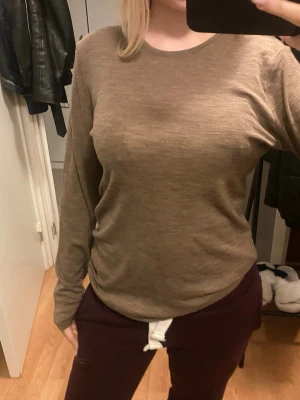 Beige långärmad tröja i ull - Säljer en enkel och stilren beige långärmad tröja i mjuk ull. Tröjan har rund hals och en normal passform som sitter skönt mot kroppen. Perfekt att bära som lager eller bara som den är. Passar dig som gillar neutrala färger och klassisk stil.