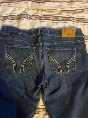 Blå jeans från Hollister W27 L33 - Snygga blå jeans från Hollister med klassisk femficksdesign och kontrastsömmar på bakfickorna. Modellen har normal passform och raka ben, med knapp och dragkedja framtill. Perfekt för dig som gillar en enkel och tidlös jeanslook.