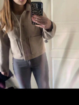 Beige overshirt med stora fickor - Säljer en beige overshirt med krage och stora fickor framtill. Jackan har en rak och lite boxig passform, stängs med knappar och är långärmad. Perfekt för lager-på-lager och enkel att styla till olika outfits.