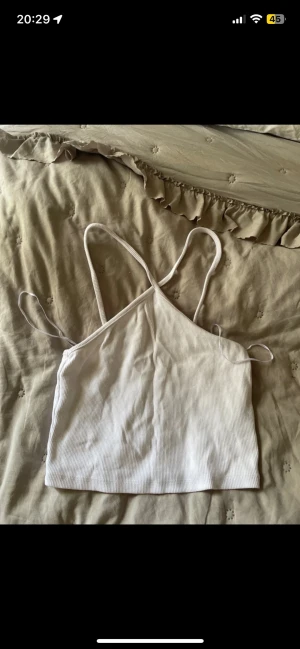 Vit ribbad linnetopp från Zara - Säljer en vit ribbad linnetopp från Zara i storlek M. Toppen har smala axelband som korsas i ryggen och är croppad i modellen. Perfekt för varma dagar och enkel att matcha med jeans eller kjol.