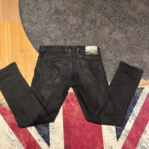Replay svarta jeans, storlek 30/32 - Jeansen har en rak/slim passform och är tillverkade i slitstarkt bomullsmaterial med en lätt glansig finish. Bilden kan vara missledande, då de inte är lika glansiga som det ser ut🙃De är iallafall perfekt för dig som letar efter att par nya jeans inför 2026. De är i ytterst bra skick, inga synliga tecken på slitage förutom på läderpatchen. Nypris: 1000kr, Mitt pris: 350✨ Skriv gärna om du har några funderingar🤗