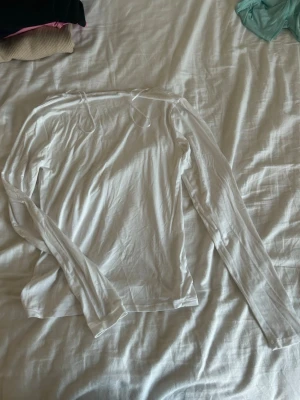 Vit långärmad topp från 157 - Säljer en enkel och stilren vit långärmad topp från 157 i storlek S. Toppen har rundad halsringning och är tillverkad i mjuk bomull som känns skön mot huden. Perfekt att matcha med jeans eller kjol för en clean look.