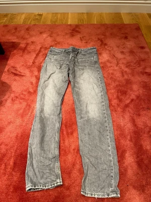 Jack and Jones - Säljer ett par klassiska Jack and Jones jeans i grå tvätt med rak passform. Byxorna har fem fickor, knappgylf och det ikoniska Levis-märket bak i midjan. Perfekt för dig som gillar en tidlös och chill stil.
