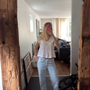 Vit blus med volang och spetsdetaljer - Säljer en luftig vit blus med v-ringning, volang vid axlarna och fina spetsdetaljer upptill. Blusen är croppad och har en lös passform, perfekt till jeans eller kjol. Gjord i tunn bomull som känns skön mot huden.