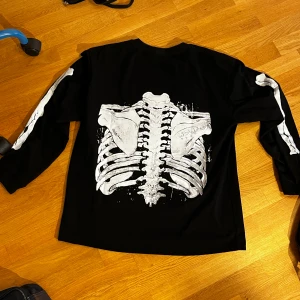 Svart långärmad tröja med skelettprint - Cool svart långärmad tröja med vitt skelettmönster både fram och bak samt på ärmarna. Perfekt för dig som gillar unika och edgy plagg. Tröjan har en avslappnad passform och är tillverkad i mjukt bomullstyg. Jätte ny hade på mig en gång.