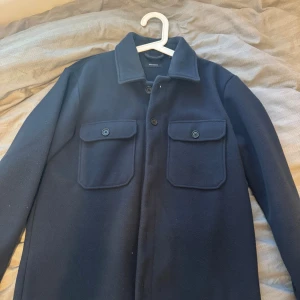 Mörkblå overshirt från Matinique L - Säljer en stilren mörkblå overshirt från Matinique i storlek L. Jackan har två stora bröstfickor med knappar, klassisk krage och knäppning framtill. Perfekt för lager-på-lager och enkel att matcha till olika outfits.