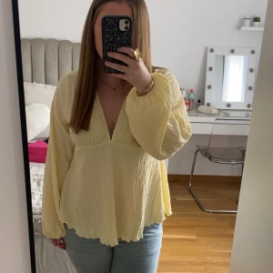 Ljusgul blus med v-ringning - Säljer en ljusgul blus med v-ringning och långa, luftiga ärmar. Blusen har en lätt skrynklig struktur och knytning i nacken. Använd 2-3 gånger. 