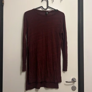 Vinröd långärmad klänning Gina Tricot - Enkel och stilren vinröd klänning från Gina Tricot med lång ärm och rund halsringning. Modellen är rak och något längre baktill, tillverkad i ett mjukt och lätt material som ger en avslappnad känsla.