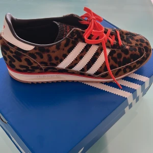 Adidas SL 72 OG W leopard sneakers - Unika Adidas SL 72 OG W sneakers med leopardmönster, röda snören och klassiska vita stripes. Ovandel i syntet med pälsliknande finish, gummisula och detaljer i vitt och rött. Perfekt för dig som vill sticka ut med en djärv stil.