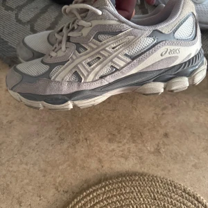 Gråvita Asics sneakers med mesh - Snygga Asics sneakers i grått och vitt med meshpaneler och detaljer i mocka. Skorna har snörning och en chunky sula som ger en sportig vibe. Perfekta för dig som gillar streetstyle och bekväma skor till vardags.