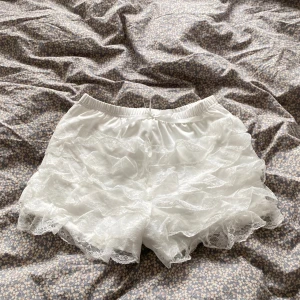Vita spetsvolang shorts - Superfina vita shorts med flera lager volanger i spets. De har elastisk midja och är gjorda i ett mjukt, lätt material som känns skönt mot huden. Perfekta för dig som gillar romantisk och söt stil med extra detaljer.