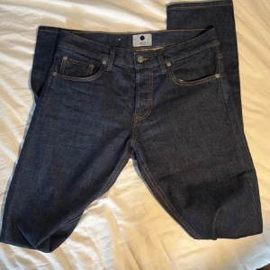 Mörkblå jeans från NN07, strl 29/34 - Snygga mörkblå jeans från NN07, modell Jeans Three. Klassisk femficksdesign med kontrastsömmar och rak passform. Jeansen är tillverkade i slitstarkt bomullsmaterial och har en stilren look som funkar till många olika outfits.