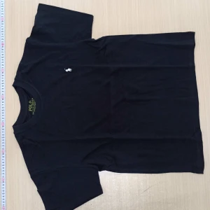 Svart t-shirt från Polo Ralph Lauren - Svart t-shirt från Polo Ralph Lauren med klassisk vit broderad logga på bröstet. Modellen är slim fit och har rund halsringning samt korta ärmar. Tillverkad i mjuk bomull för en skön känsla och stilren look.