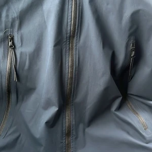 Svart vindjacka C.P. Company - Snygg svart vindjacka från C.P. Company med flera dragkedjor och coola detaljer. Jackan är gjord i stretchig polyester med WR coating, vilket gör den perfekt för blåsiga dagar. Röd PRO-TEK patch på insidan ger extra streetkänsla.