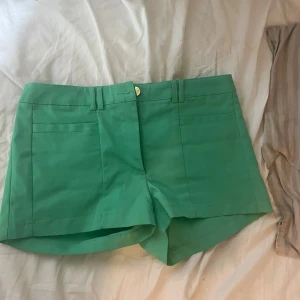 Gröna shorts från H&M, strl 36 - Snygga gröna shorts från H&M i storlek 36. De har en klassisk passform med hällor för bälte, fickor både fram och bak samt stängs med knapp och dragkedja. Perfekta för varma dagar och lätta att matcha med olika toppar.