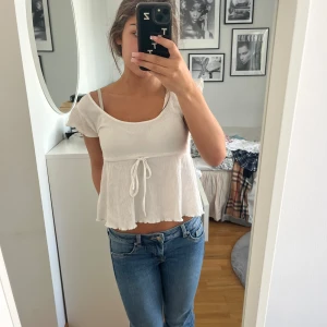 Vit croppad linnetopp med knyt från Nelly - Säljer en söt vit croppad linnetopp med korta ärmar och knyt i midjan. Toppen är från Nelly i storlek M men jag har oftast S och den sitter fint på mig! 