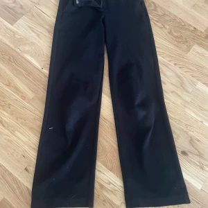 Svarta kostymbyxor från Vero Moda - Svarta kostymbyxor från Vero Moda med raka ben och normal passform. Byxorna har dragkedja och knapp framtill samt hällor för bälte. Snygg klassisk look som funkar till många olika stilar. Materialet är mjukt och känns bekvämt mot huden.