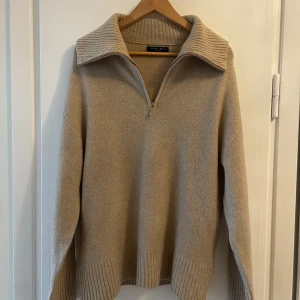 Beige stickad tröja med half zip  - Beige stickad tröja med bred ribbad krage och half zip-dragkedja. Man kan anpassa kragen utefter hur man vill ha den! Tröjan har långa ärmar och breda ribbade muddar vid ärmslut och nederkant som är lite vidare. .