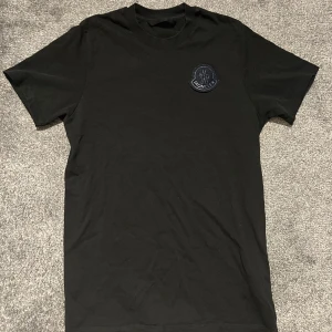 Svart Moncler t-shirt med patch - Svart t-shirt från Moncler som är köpt på room 1006 på emporia för 2999kr                                                                             Tröjan är i mycket bra skicka endast qr-koden som är lite urtvättad!