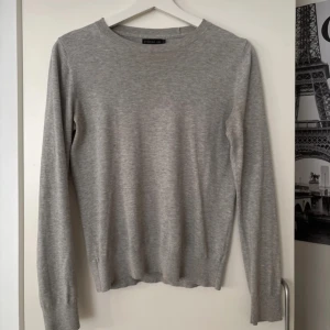 Ljusgrå stickad tröja från Stockh LM - En stilren ljusgrå stickad tröja från Stockh LM i storlek XS. Tröjan har rund halsringning, långa ärmar och en diskret metallring som detalj i nacken. Perfekt basic-plagg med mjuk känsla och normal passform.