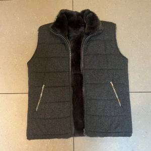 Mörkgrå pälsväst från N.Peal London - Snygg mörkgrå pälsväst från N.Peal London i storlek M. Utsidan är quiltad och gjord av 100% kashmir, medan insidan har mjuk och lyxig brun kaninpäls. Västen har två fickor med dragkedja och en hög krage som ger extra värme. Extremt bra skick och väldigt svår att få tag på. Följer med en box ifrån där den är köpt. Nypris 19,000kr. Hör av er vid frågor 