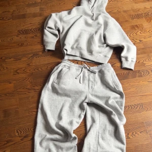 Grå tracksuit från Pull&Bear - Säljer en klassisk ljusgrå tracksuit från Pull&Bear. Tröjan har huva med dragsko, magficka och ribbade muddar. Perfekt för chill dagar eller när du vill vara extra bekväm. Materialet är mjukt och känns riktigt skönt mot huden. Hoodien är storlek S och Byxorna är storlek L. Kan köpas separat ba skriv till mig direkt.