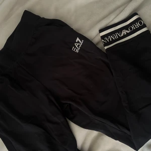 Svarta mjukisbyxor från Emporio Armani - Svarta mjukisbyxor från Emporio Armani EA7 med bred resår i midjan och logga på benet. Byxorna har en sportig look och är tillverkade i mjukt material som känns skönt mot huden. Perfekta för en avslappnad stil.