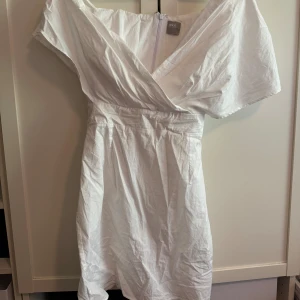 Vit omlottklänning från ASOS - Snygg vit kortklänning från ASOS med omlott framtill och v-ringning. Klänningen har korta ärmar och ett knytband i midjan.
