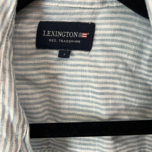 Lexington linneskjorta - Säljer en snygg blå- och vitrandig skjorta från Lexington i 100% linne. Skjortan har klassisk krage, bröstficka och knäppning framtill. Perfekt för en chill och stilren look under varmare dagar.